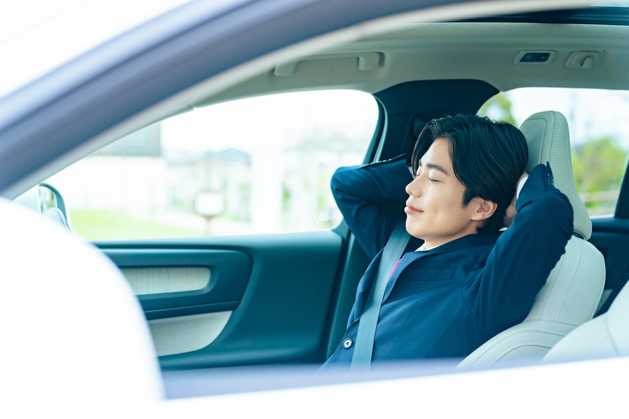 車内でシートに深く寄りかかり、目を閉じてリラックスしている男性