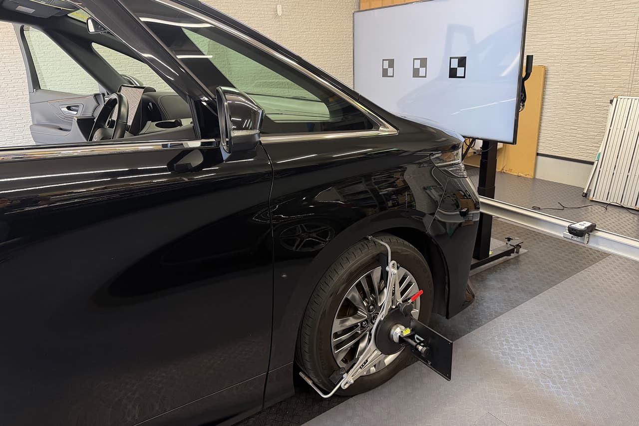 車両の前方にターゲットボードのモニターを配置し、タイヤに専用機器を取り付けてエーミング調整を行っている様子